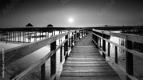 perspective of wood bridge in deep sea crossing water stream and glowing light at the end of wooden ways