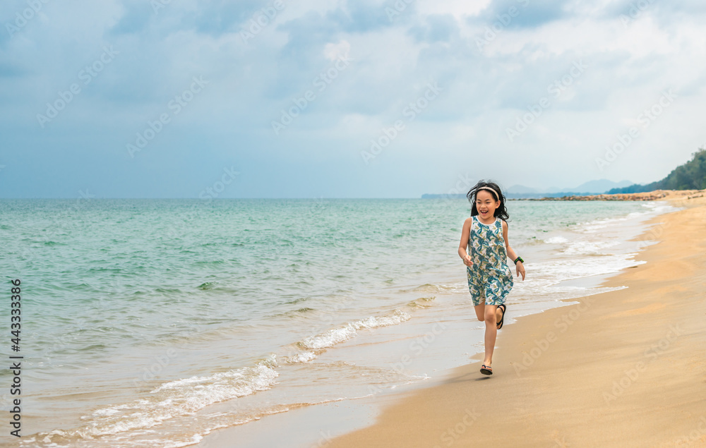 Asian little girl running on the beautiful beach, smiling face, black long hair, 7 years old, turquoise color ocean and blue sky. Blank space for text and design.