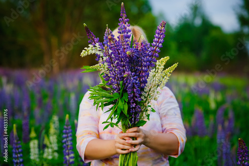 Portrait of a beautiful plus-size blonde with a bouquet of lilac-purple lupine flowers in her hands. A stout woman stands on a blooming meadow.