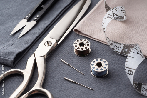 Scissors, spools of thread, needles, and a centimeter lie on the dark gray fabric of the T-shirt. Sewing accessories on the background of sewn clothes. Cutting and sewing concept. Tailor's Desk
