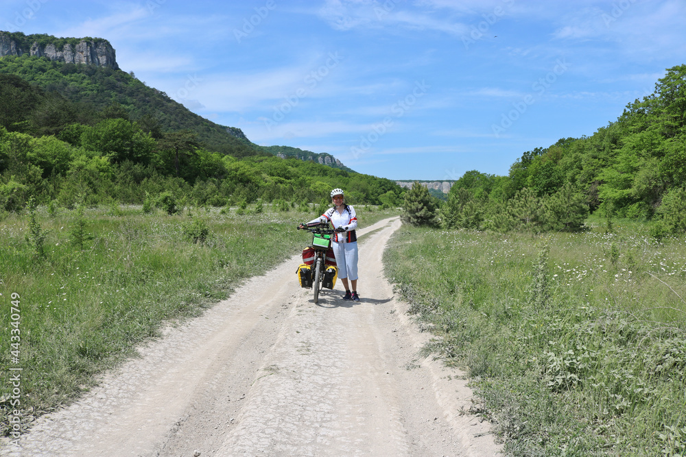 A happy cyclist leads her bike along a high plateau among the mountains. Summer landscape, summer bike trip. Mangup-Kale, Crimea.