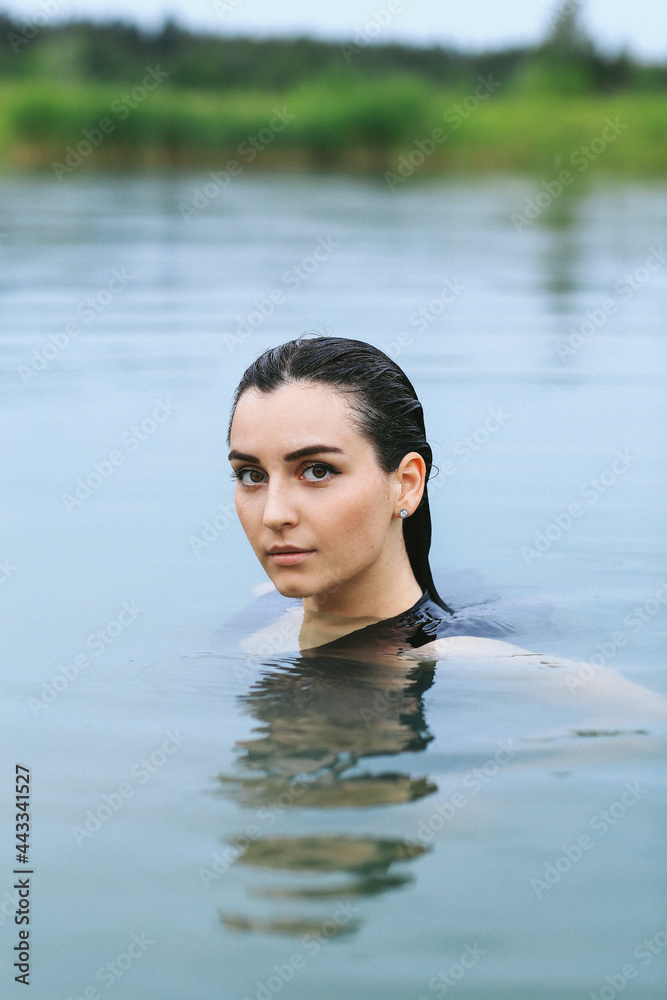 Fototapeta premium A dark-haired girl swims in the lake and takes a photo session