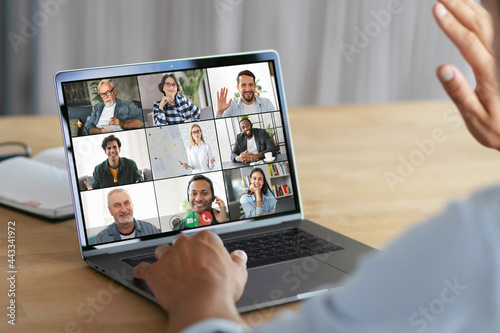 Online meeting, group brainstorming concept. Successful man waving his hand at the laptop computer screen, greeting employees during an video conference