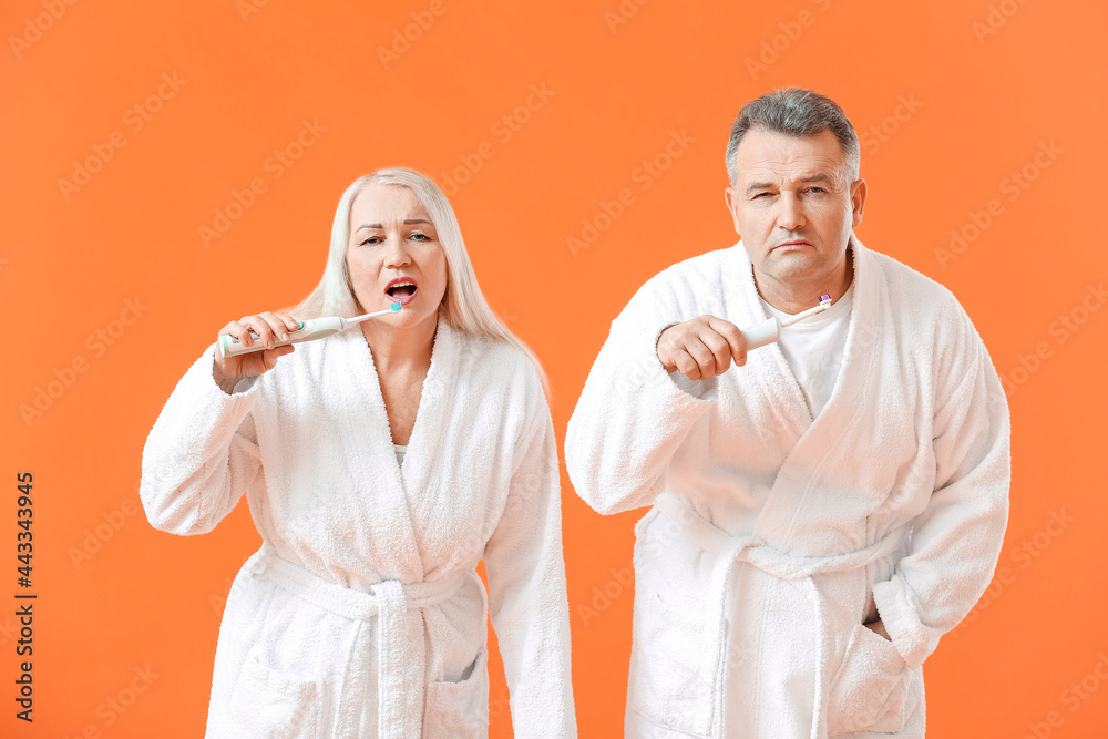 Mature couple brushing teeth on color background Mature couple brushing teeth on color background