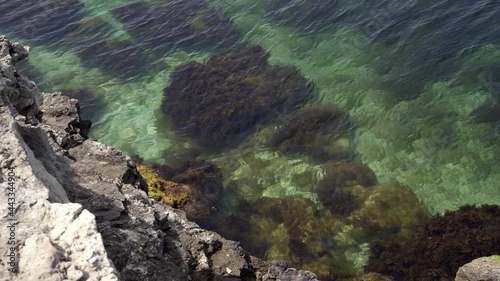 The bottom is visible through the clear water. Clear sea next to the rocky coast. Top view, slow motion, HD. photo