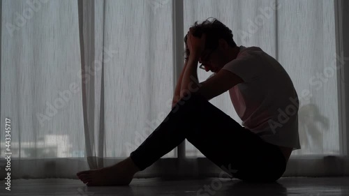 Desperate man sitting with hands on his head on the floor beside windows for stress and depression concept.