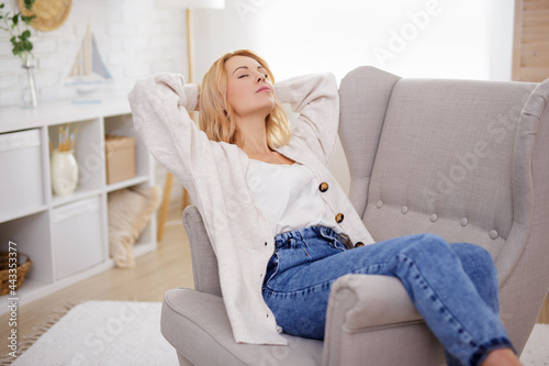 home, cosiness and relaxation concept - young beautiful woman resting on armchair in bright living room