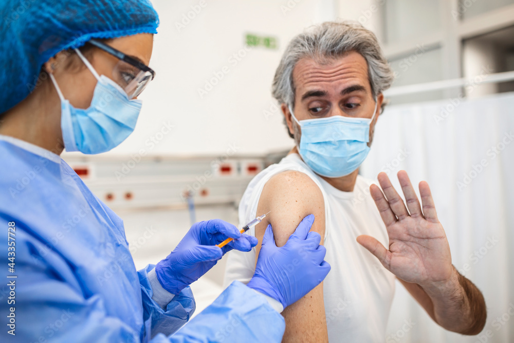 Professional doctor or nurse giving flu or COVID-19 injection to patient. Man in medical face mask getting antiviral vaccine at hospital or health center during vaccination and immunization campaign Professional doctor or nurse giving flu or COVID-19 injection to patient. Man in medical face mask getting antiviral vaccine at hospital or health center during vaccination and immunization campaign