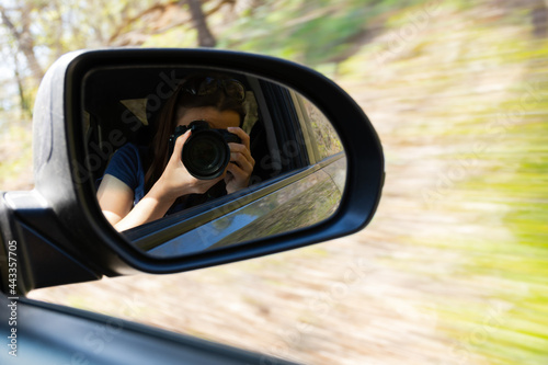 Woman camera selfie car. A young woman is traveling by car and takes pictures of herself in the side mirror. The concept of speed, movement, travel. Modern lifestyle. Blurred motion nature background