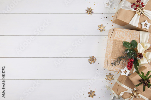 Border of gift boxes wrapped in kraft paper decorated with red berries, white ribbons and Christmas greenery on white wood desk background Xmas, winter, holiday concept. Flat lay, top view, copy space © Aleksandra Konoplya