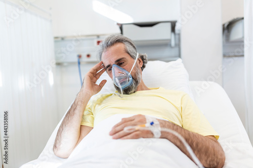 Male coronavirus patient looking away while resting on hospital bed. Man is wearing oxygen mask. He is in hospital during pandemic.
