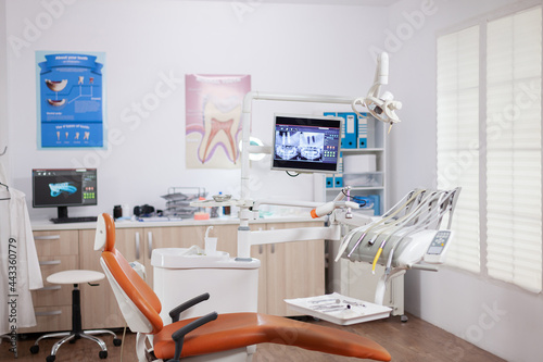 Dental chair and other accesorries used by dentist in empty cabinet. Stomatology cabinet with nobody in it and orange equipment for oral treatment.