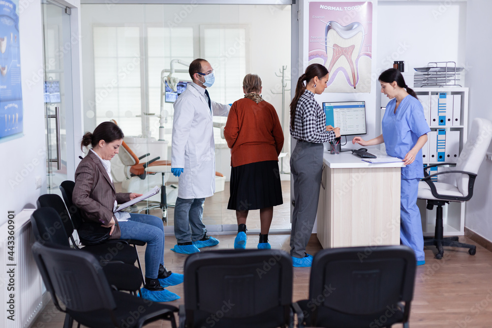 Young lady asking informations filling in stomatological form while patients talking sitting on chair in waiting area. People speaking in crowded professional orthodontist reception office. Young lady asking informations filling in stomatological form while patients talking sitting on chair in waiting area. People speaking in crowded professional orthodontist reception office.