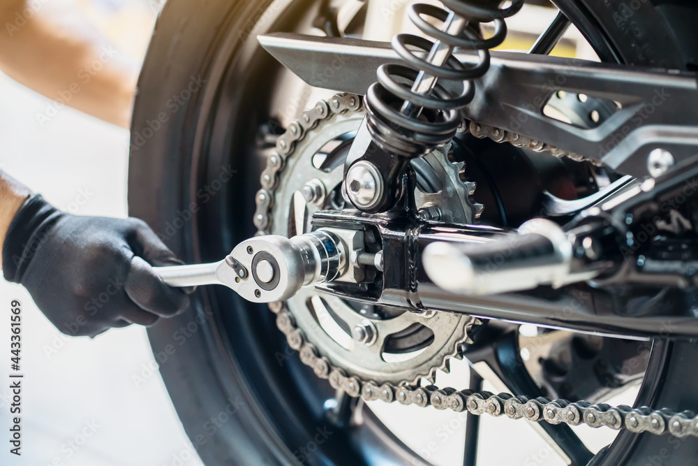 Mechanic using a wrench and socket to Remove and Replace Rear Motorcycle Wheel , maintenance, repair motorcycle concept in garage .selective focus