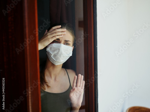 woman in medical mask looking out the window sad look