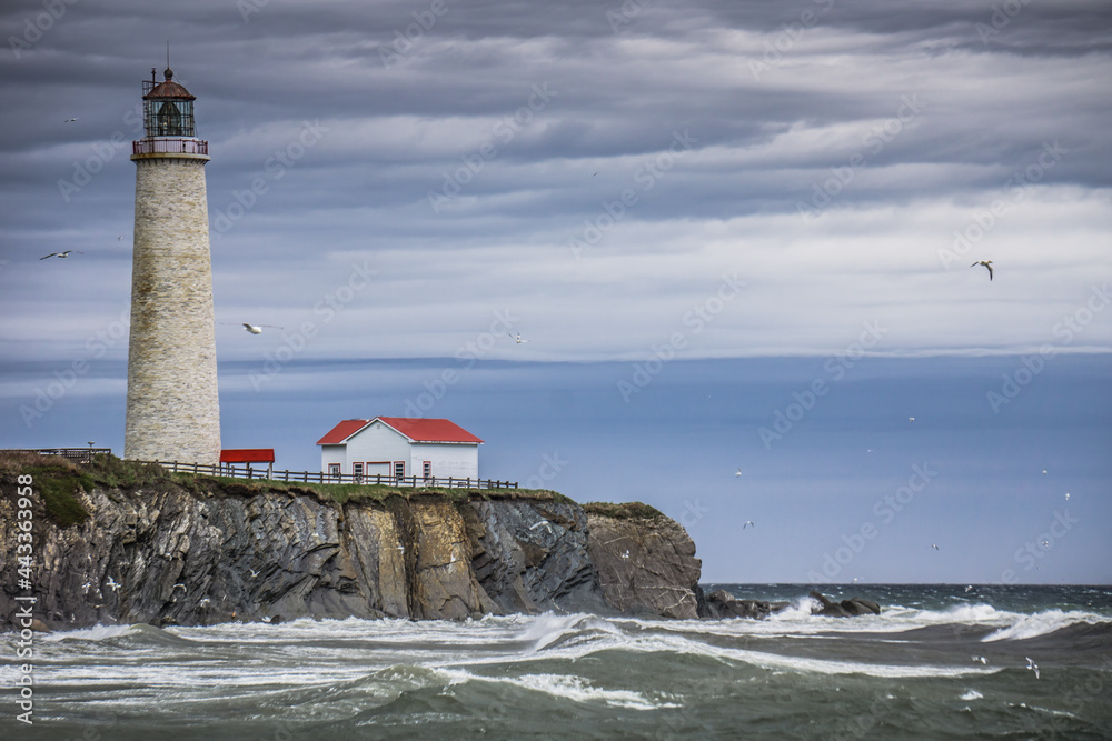 View on the turbulent sea, the cliffs and the Cap des Rosiers lighthouse on a cloudy and moody day (Quebec, Canada)