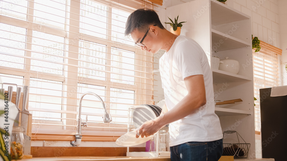 Happy young Asia guy washing dishes while doing cleaning in the kitchen at house. Stay at home, self isolation, social distancing, quarantine for coronavirus, lifestyle man at home concept. Happy young Asia guy washing dishes while doing cleaning in the kitchen at house. Stay at home, self isolation, social distancing, quarantine for coronavirus, lifestyle man at home concept.