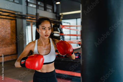 Young Asia lady kickboxing exercise workout punching bag tough female fighter practice boxing in gym fitness class. Sportswoman recreational activity, functional training, healthy lifestyle concept.