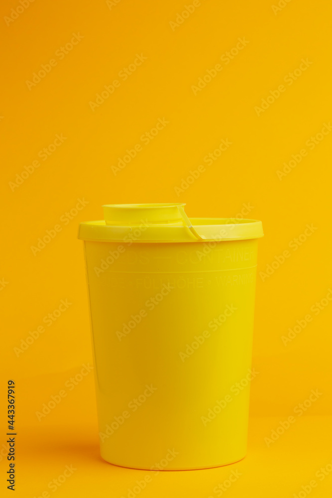 Front view of container with round cap on seamless yellow background for the disposal of used injector needles with drug residue. Studio medical equipment still life concept. Front view of container with round cap on seamless yellow background for the disposal of used injector needles with drug residue. Studio medical equipment still life concept.
