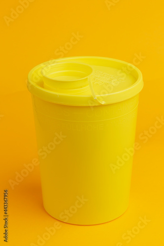 Top lit of container with round cap on seamless yellow background for the disposal of used injector needles with drug residue. Studio medical equipment still life concept. photo