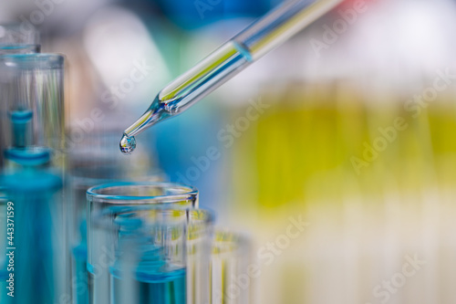Drop of blue liquid from droper droping to test tube in laboratory with bright color blur background