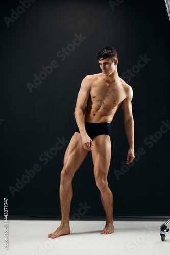 man with a pumped up naked body in black panties posing against a dark background