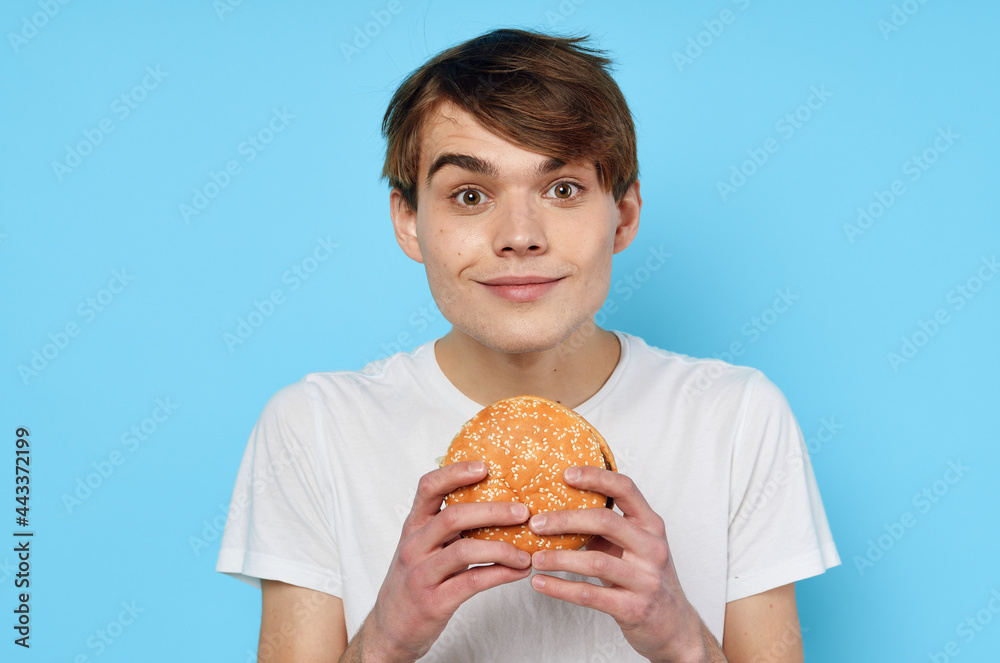 Man eating hamburger in white t-shirt diet food lifestyle blue background Man eating hamburger in white t-shirt diet food lifestyle blue background