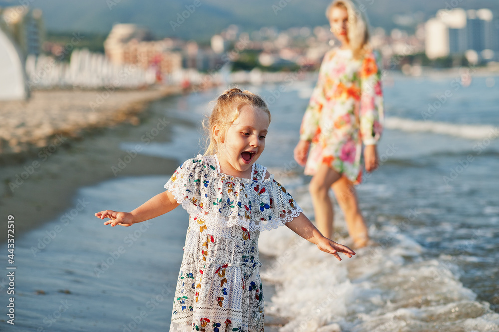 Naklejka premium Mother and beautiful daughter having fun on the beach. Portrait of happy woman with cute little girl on vacation.