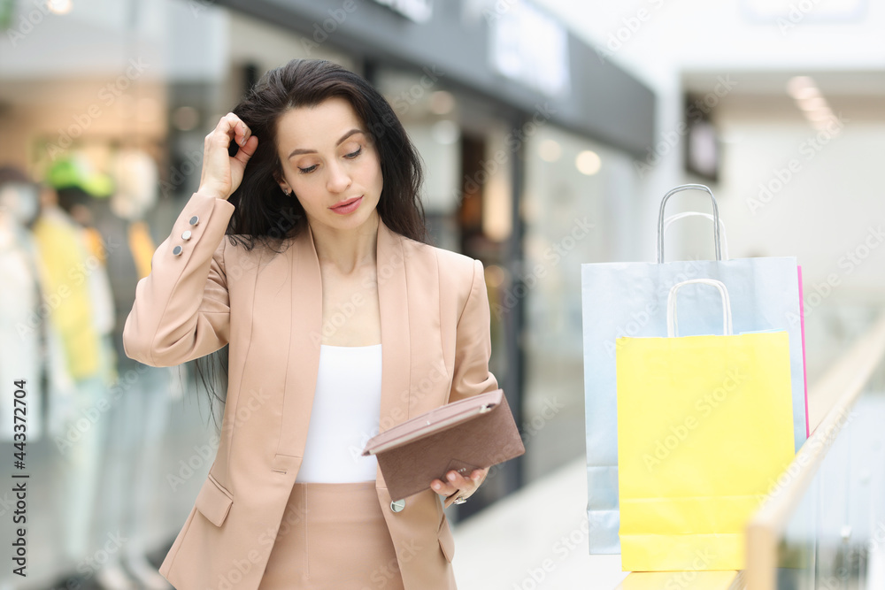 Fototapeta premium Young woman in suit looking into empty wallet in shopping center