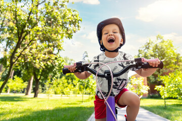 Portrait little cute adorable caucasian toddler boy in safety helmet enjoy having fun riding exercise bike in city park road yard garden forest. Child first bike. Kid outdoors sport summer activities