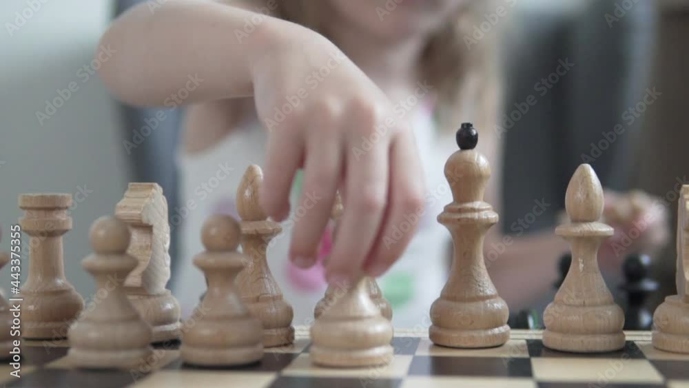 A close-up of the chessboard, the girl puts the pawns on the chessboard. The baby in the background is blurred. A close-up of the chessboard, the girl puts the pawns on the chessboard. The baby in the background is blurred.