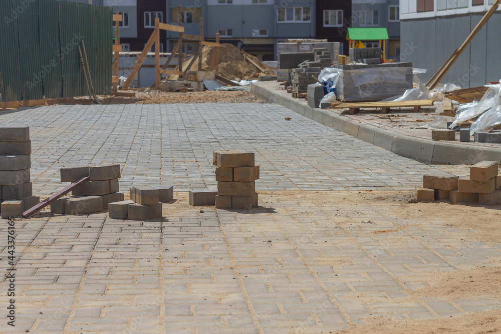 Laying paving slabs on the sidewalk in the city near a new house under construction