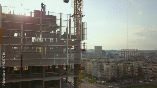 Raising a cistern with concrete on the roof of a high-rise building under construction with workers in helmets against the backdrop of city life, in the backlight