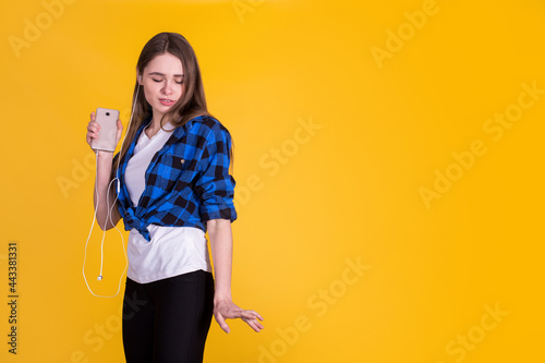 Beautiful fascinating girl in a blue shirt listening music and dancing on a yellow background