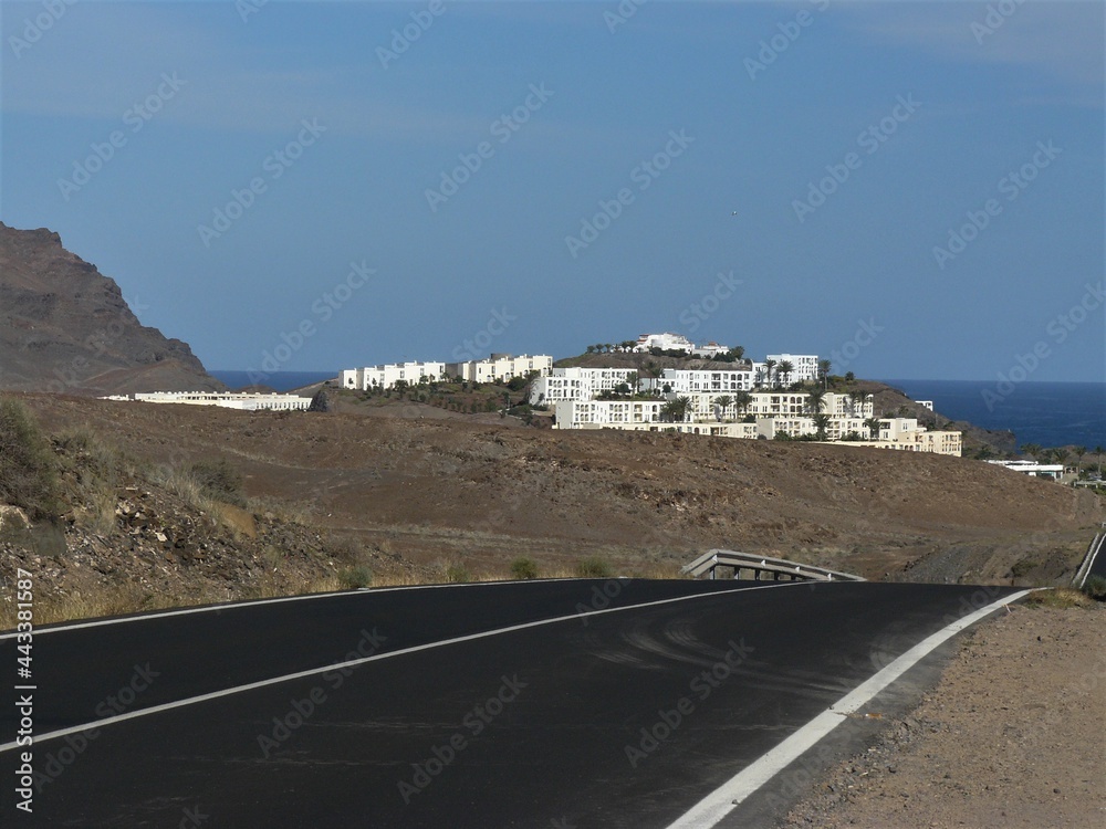 Strasse durch die Felslandschaften mit Häusern von Las Playitas / Fuerteventura im Hintergrund 