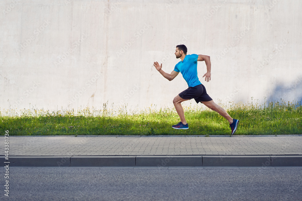 Athletic man running in city isolated against concrete wall