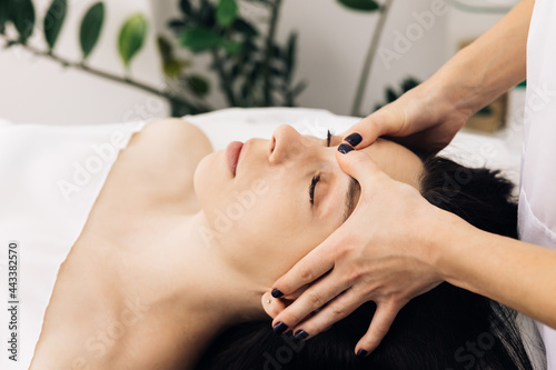 Caucasian woman lying on spa bed get facial massage treatment with aroma essential oil skincare from massage therapist at beauty salon. Wellness body massage and face spa concept.