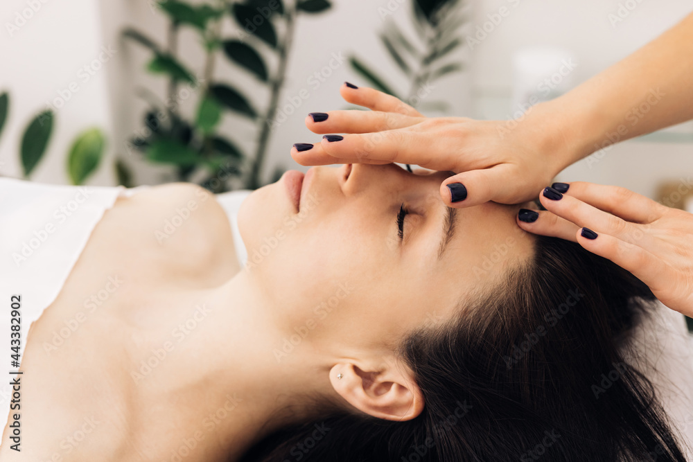 Fototapeta premium Woman lying on spa bed get facial massage treatment with aroma essential oil skincare from massage therapist at beauty salon. Wellness body massage and face spa concept.