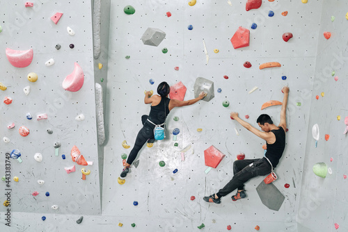 Strong young couple training in bouldering facility, they are climbing on artificial wall indoors