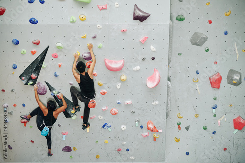 Young athletes training indoors and climbing on bouldering wall, view from above