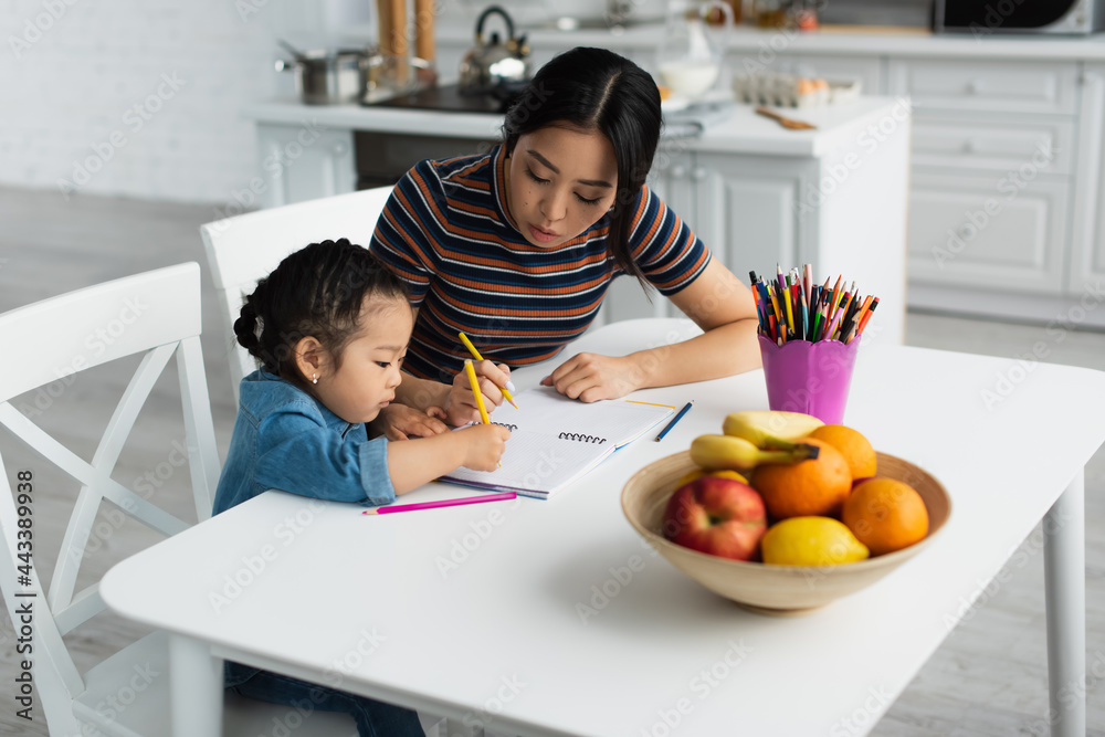 Asian mother drawing with child near fruits on table Asian mother drawing with child near fruits on table