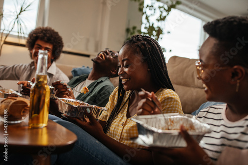 Group of young friends enjoying takeout food at home during weekend