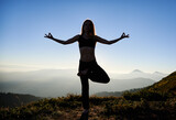 Young woman practicing yoga on background of evening mountains. Meditating female is balancing on one leg after sunset. Concept of healthy lifestyle.