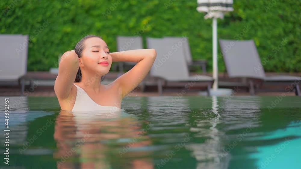 Sexy asian woman standing in a swimming pool water half submerged, closing her eyes looking up and touching her wet hair enjoying her summer holidays. Sexy asian woman standing in a swimming pool water half submerged, closing her eyes looking up and touching her wet hair enjoying her summer holidays.