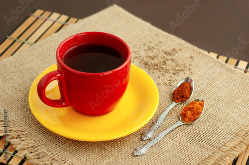 Чай с перцем и куркумой. Красная чашка чая, желтое блюдце, перец и куркума на мешковине. Чай со специями для здорового образа жизни.