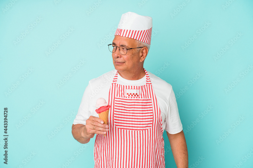 Senior american ice cream maker holding an ice cream isolated on blue background confused, feels doubtful and unsure. Senior american ice cream maker holding an ice cream isolated on blue background confused, feels doubtful and unsure.