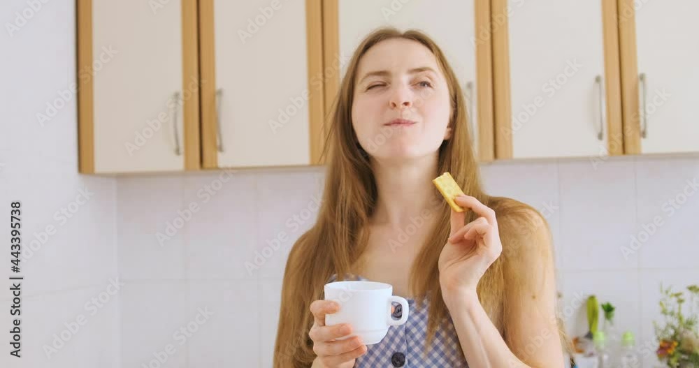 Girl is drinking tea with cookies and smiling pretty. Young woman is eating cracker and enjoying life. Cheat meal.