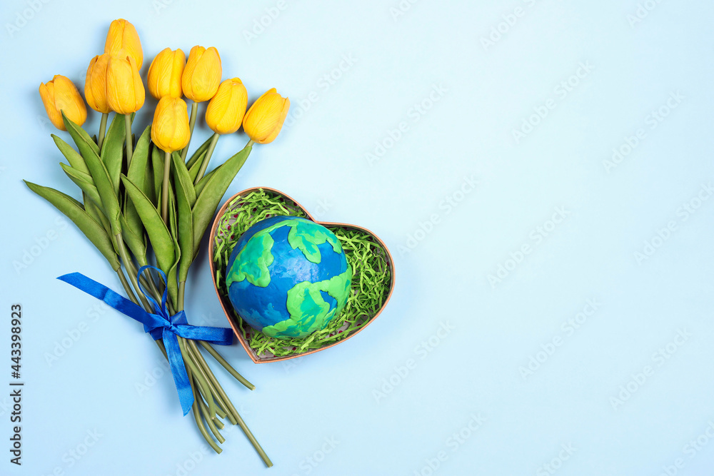 Planet Earth in a heart gift box with a bouquet of yellow tulips on a blue background. Copy space for text. Earth Day concept.