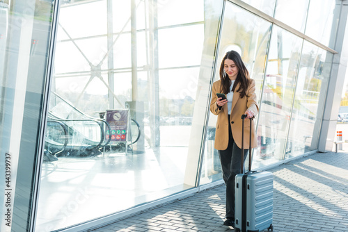 Businesswoman on commute transit typing on the smartphone while walking with hand luggage in a train station or airport going to the boarding gate. Asian woman happy using a mobile phone app for conve