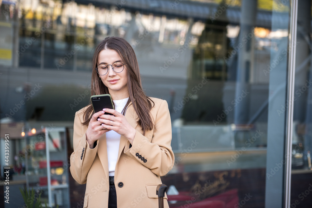 Portrait of traveling business woman with smartphone and luggage waiting on platform.